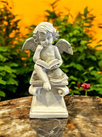 Engelfigur sitzend auf Stein mit Buch in Grau